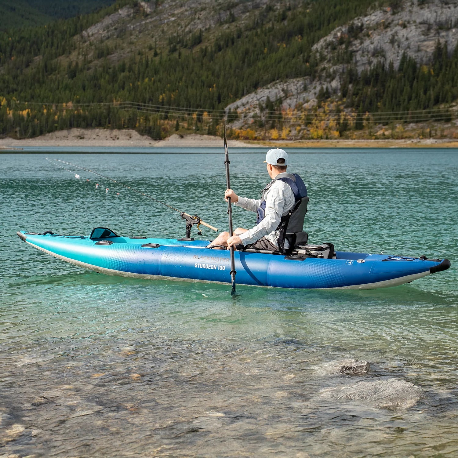 Person kayaking on a clear lake with mountains in the background
