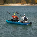 Two people in a blue kayak on a lake with trees in the background