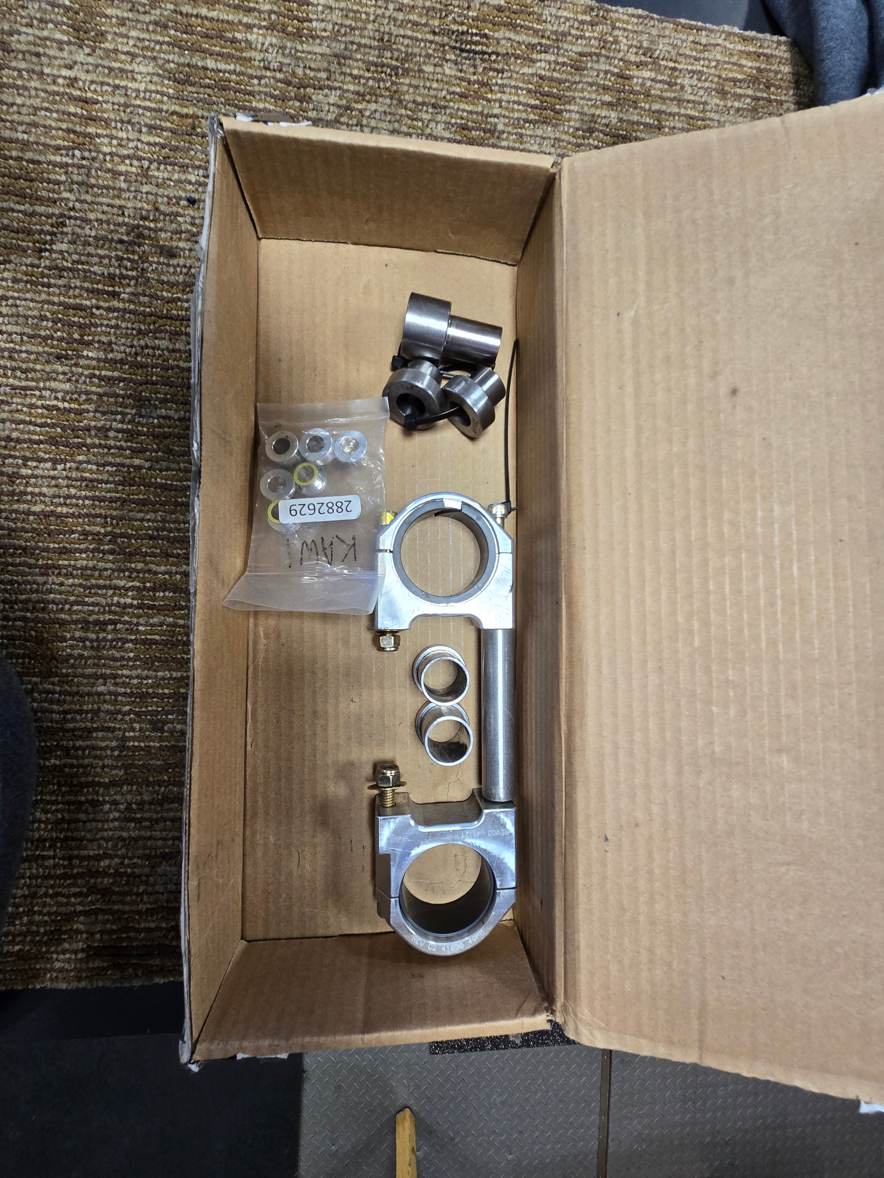 Metal mechanical parts in a cardboard box on a carpeted floor