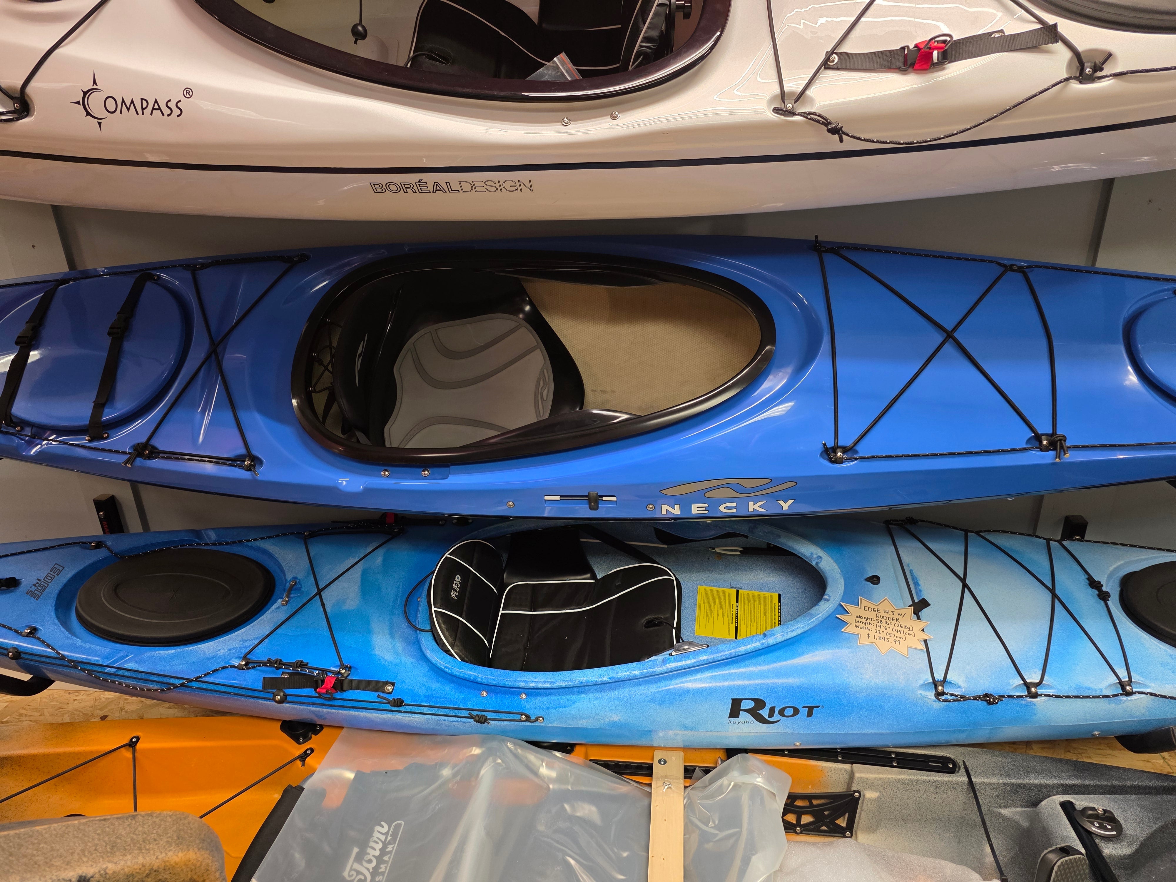Stack of kayaks with visible branding on a wooden floor.