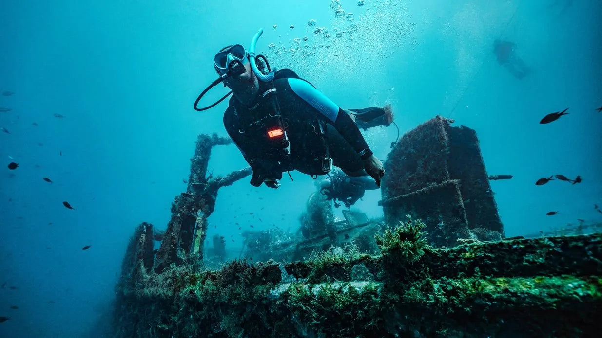 Diver exploring an underwater shipwreck with fish swimming around.