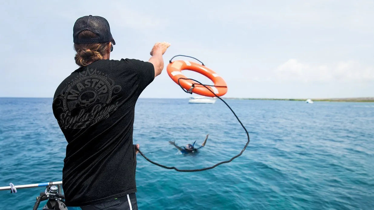 Person holding a life buoy over water with another person in the water.