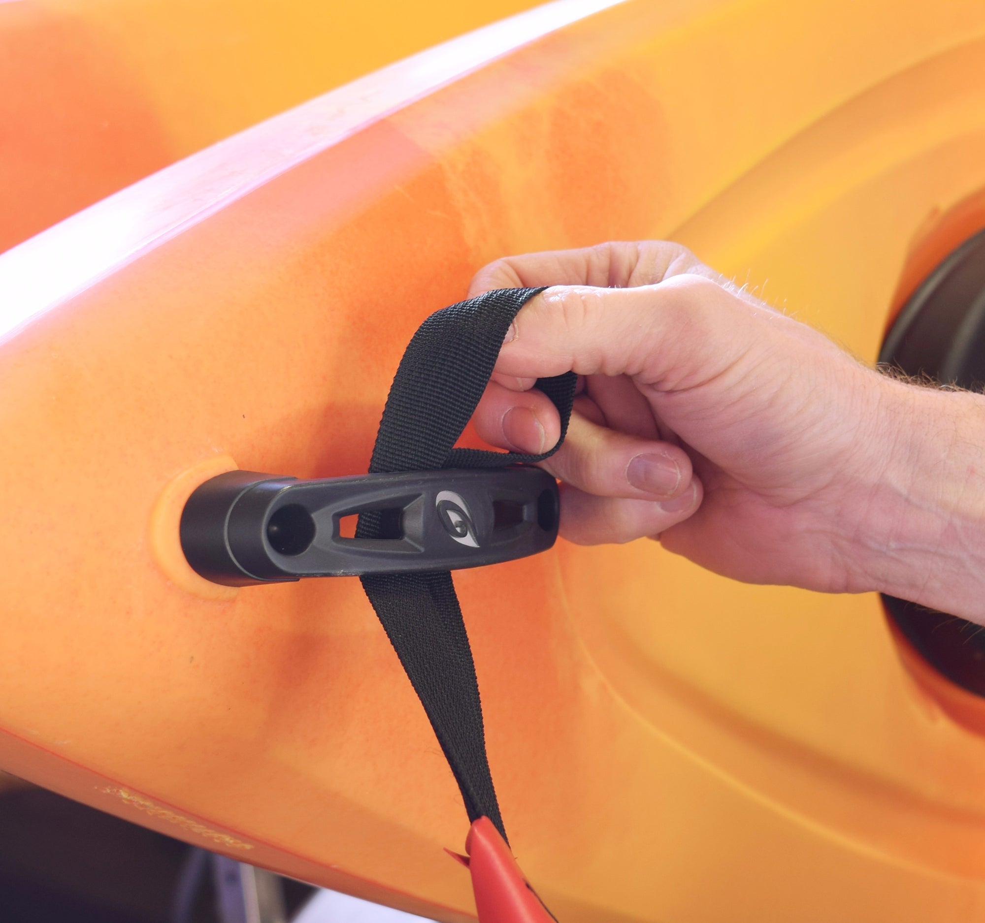 Hand securing a strap to an orange kayak