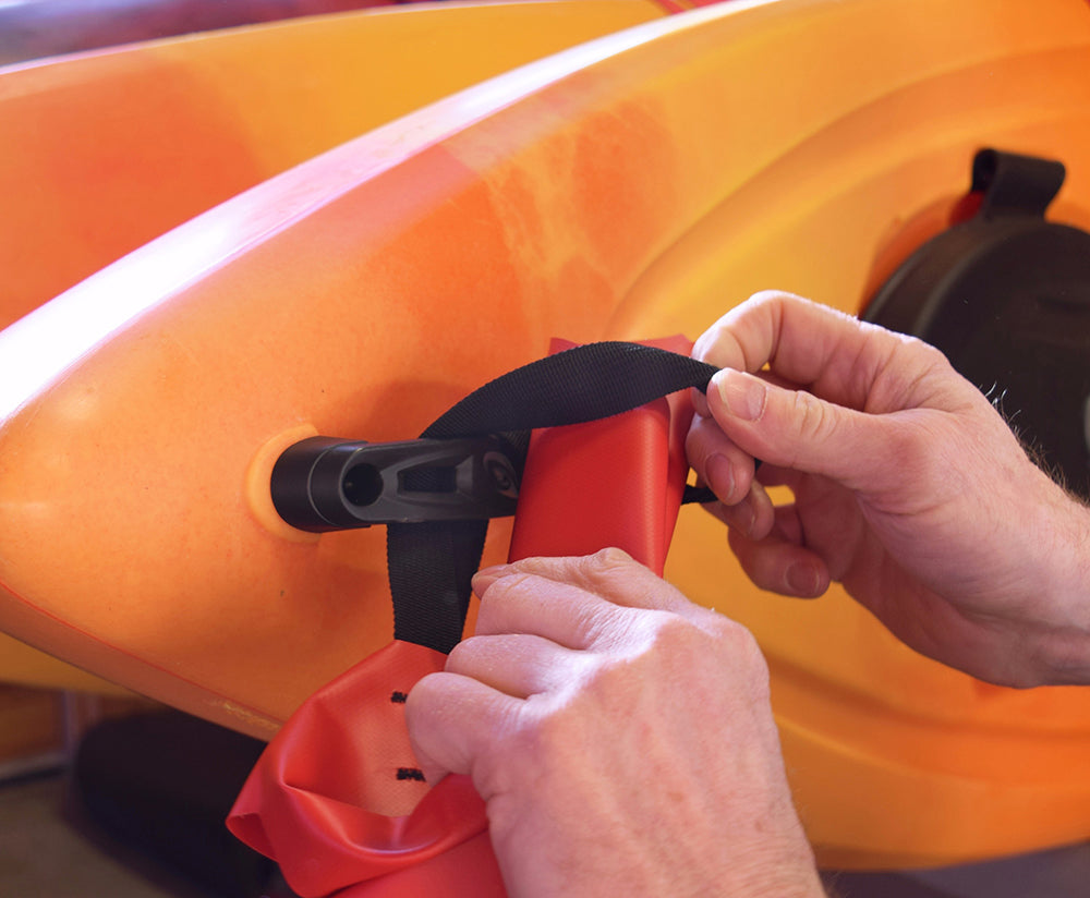 Person attaching a red lifejacket to an orange kayak.