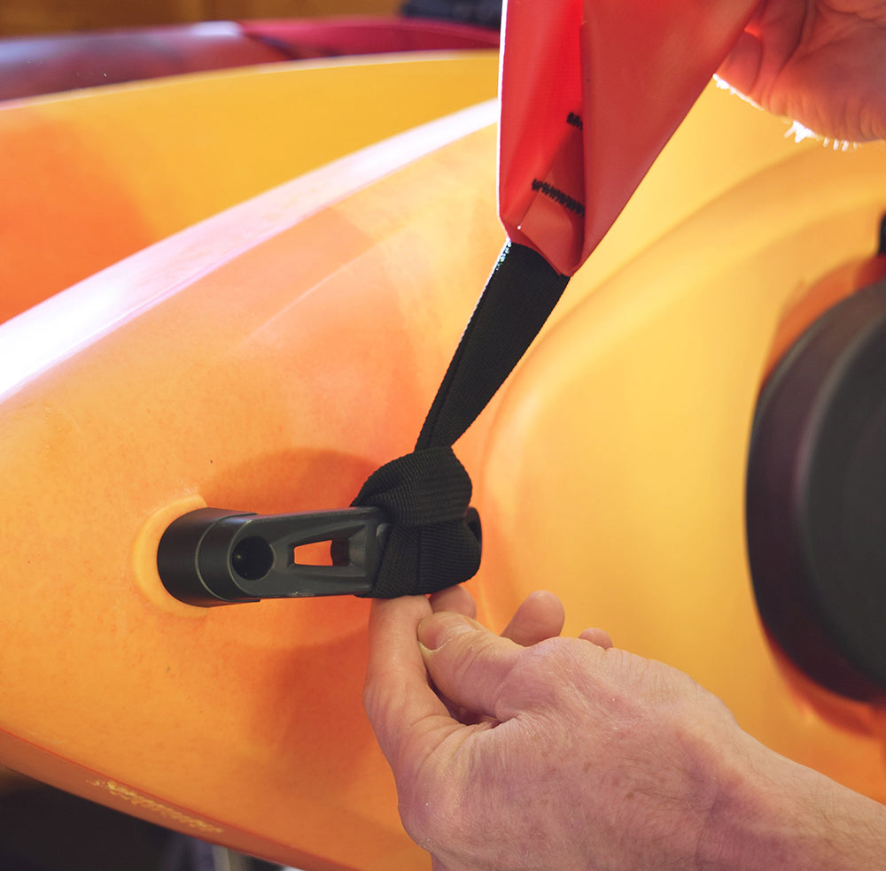 Person securing a strap to an orange inflatable kayak with a red cover.