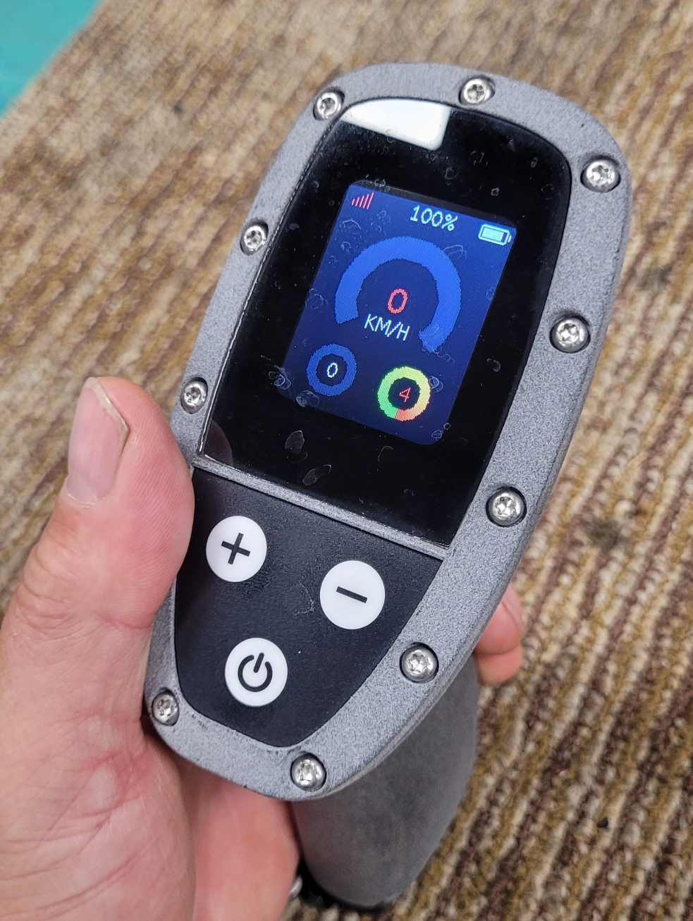 Hand holding a small electronic device with a screen and buttons on a wooden surface