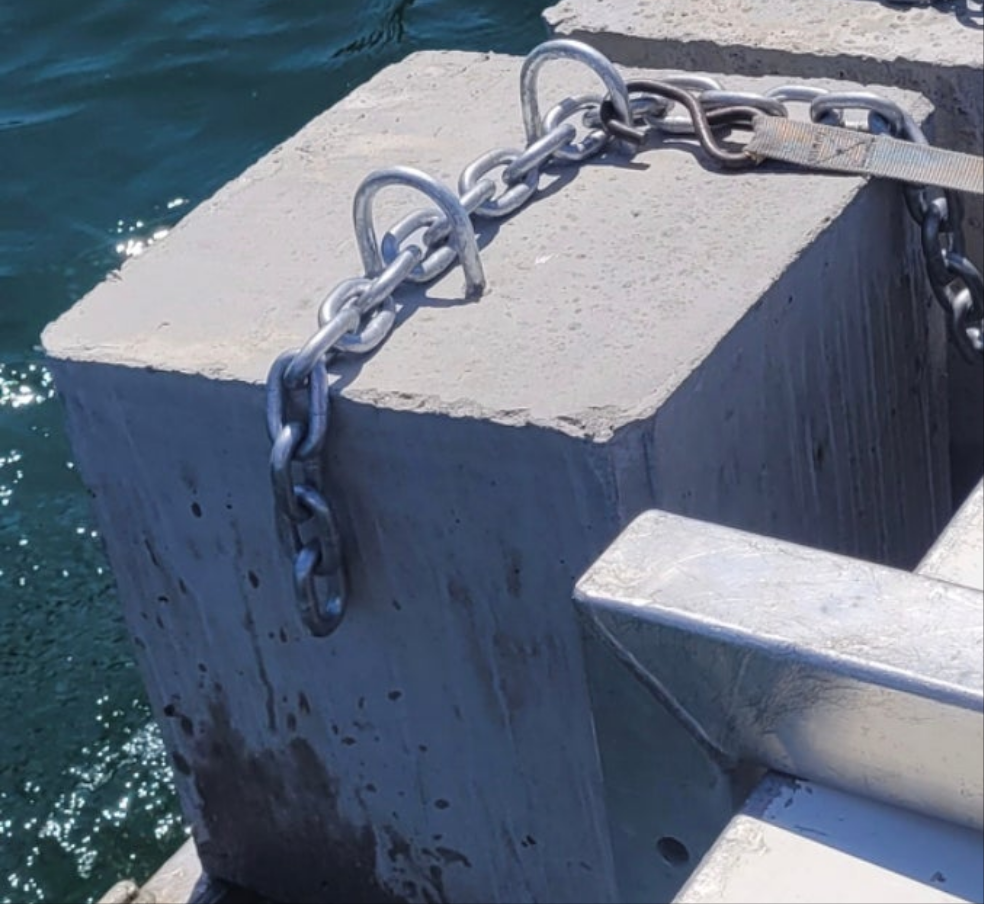 Metal chain attached to a concrete block by a body of water