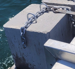 Metal chain attached to a concrete block by a body of water