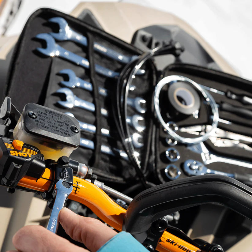 Close-up of a person holding a tool next to a set of wrenches in a case, with a motorcycle in the background.