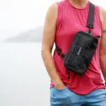 Person holding a black crossbody bag against a white background