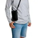 Person wearing a gray long-sleeve shirt and blue jeans with a black crossbody bag on a white background