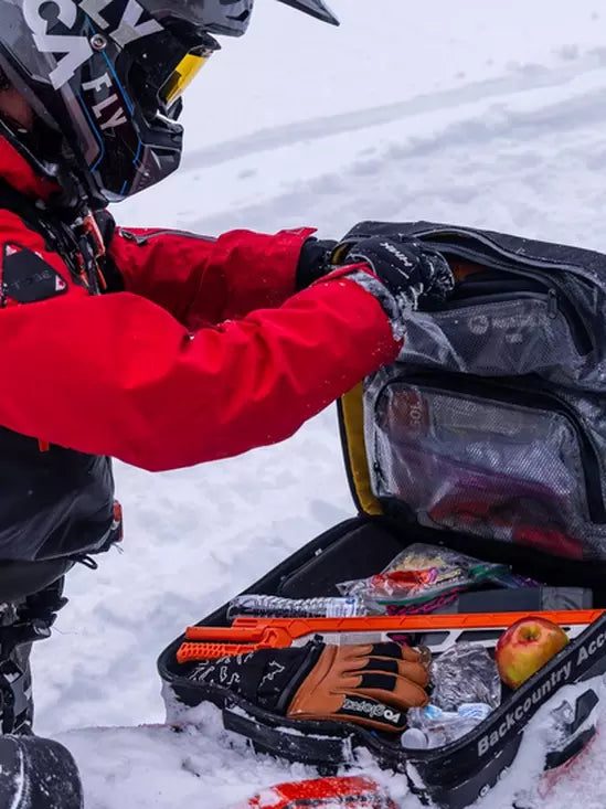 Person in red jacket with snowmobile tool box and gear in snowy environment