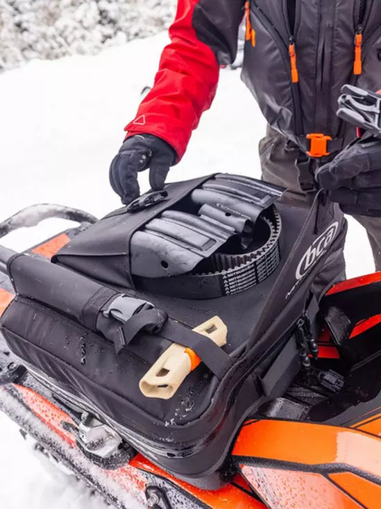Person adjusting a black snowmobile seat in a snowy environment