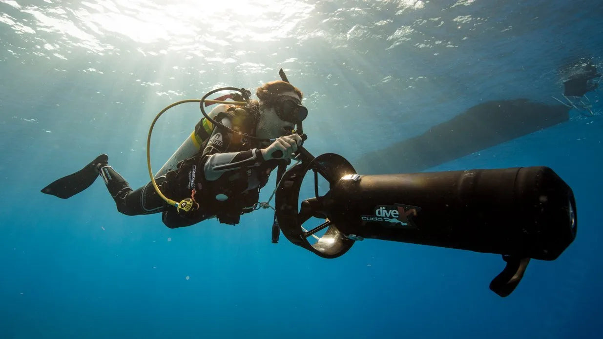 Scuba diver with a large underwater camera housing in clear blue water.