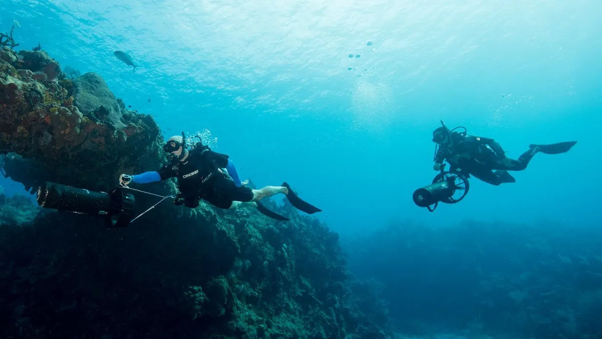 Two scuba divers exploring underwater scenery with coral and rocks.
