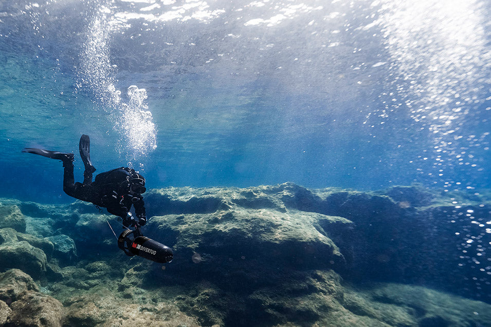Diver swimming underwater with sunlight filtering through the water