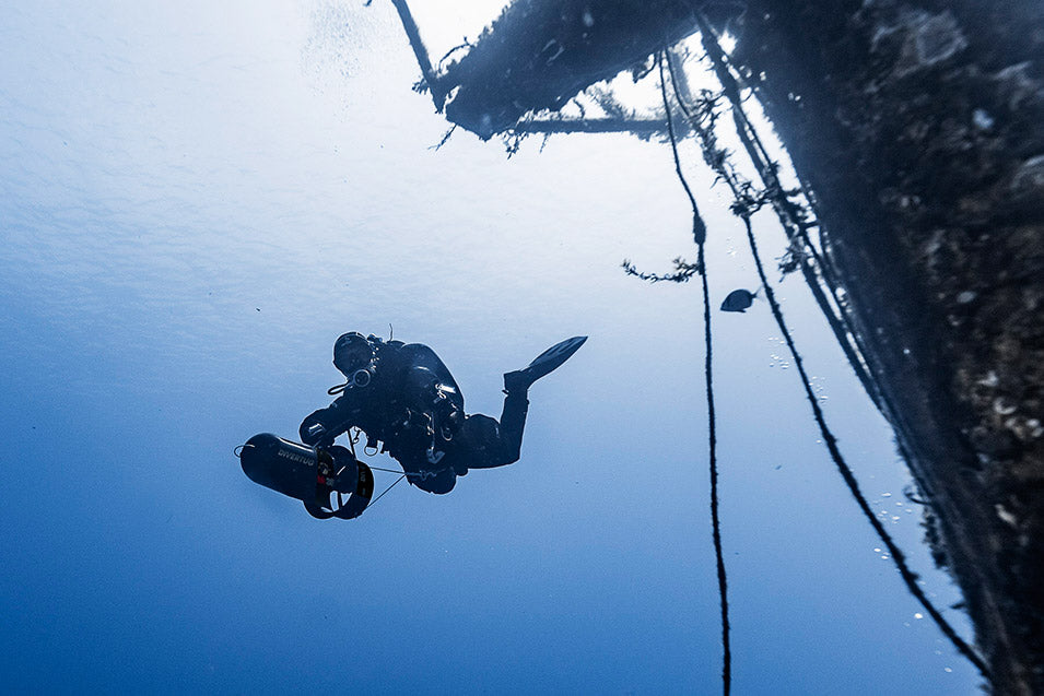 Diver underwater with a rope and equipment, looking up towards the surface.