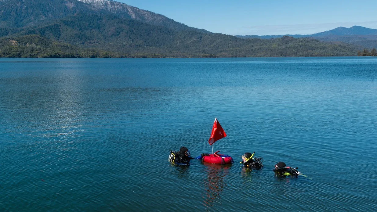 Red flag on a raft with scuba divers in the water, surrounded by mountains and clear blue sky.