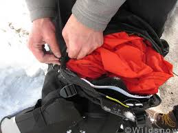 Person packing a red jacket into a black backpack with a snowy background