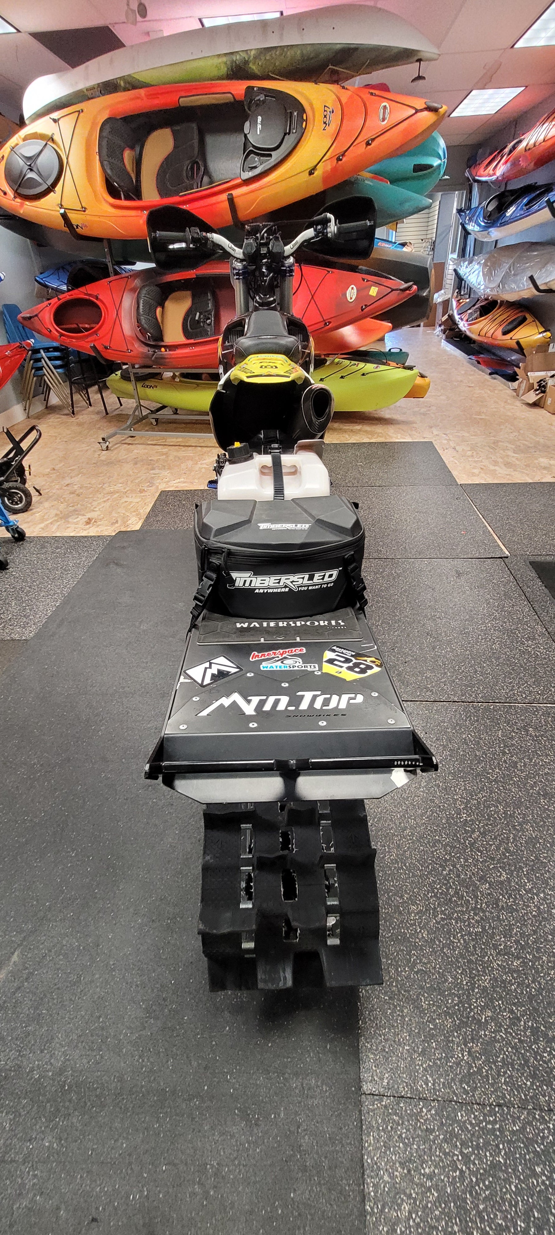 Collection of kayaks and paddle boards on a gray floor with a wall in the background