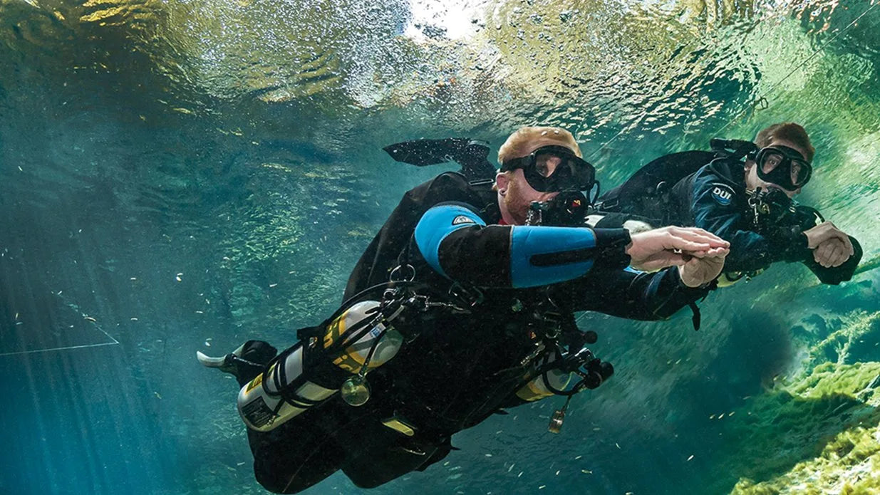 Two scuba divers underwater with clear blue water and greenery.