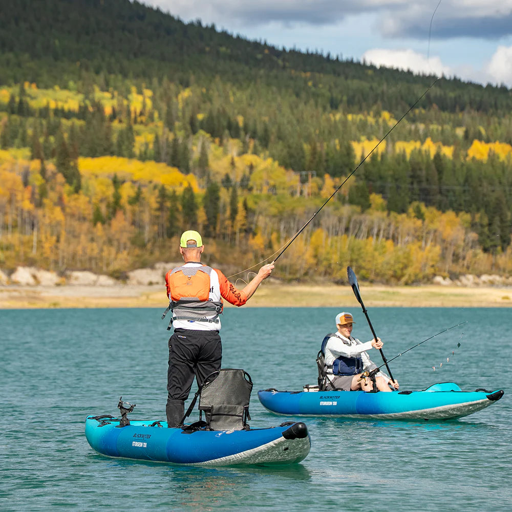 Two people in kayaks on a lake with a scenic background of trees and mountains.
