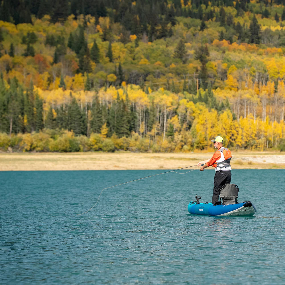 Person on a blue inflatable kayak fishing on a lake with autumn trees in the background
